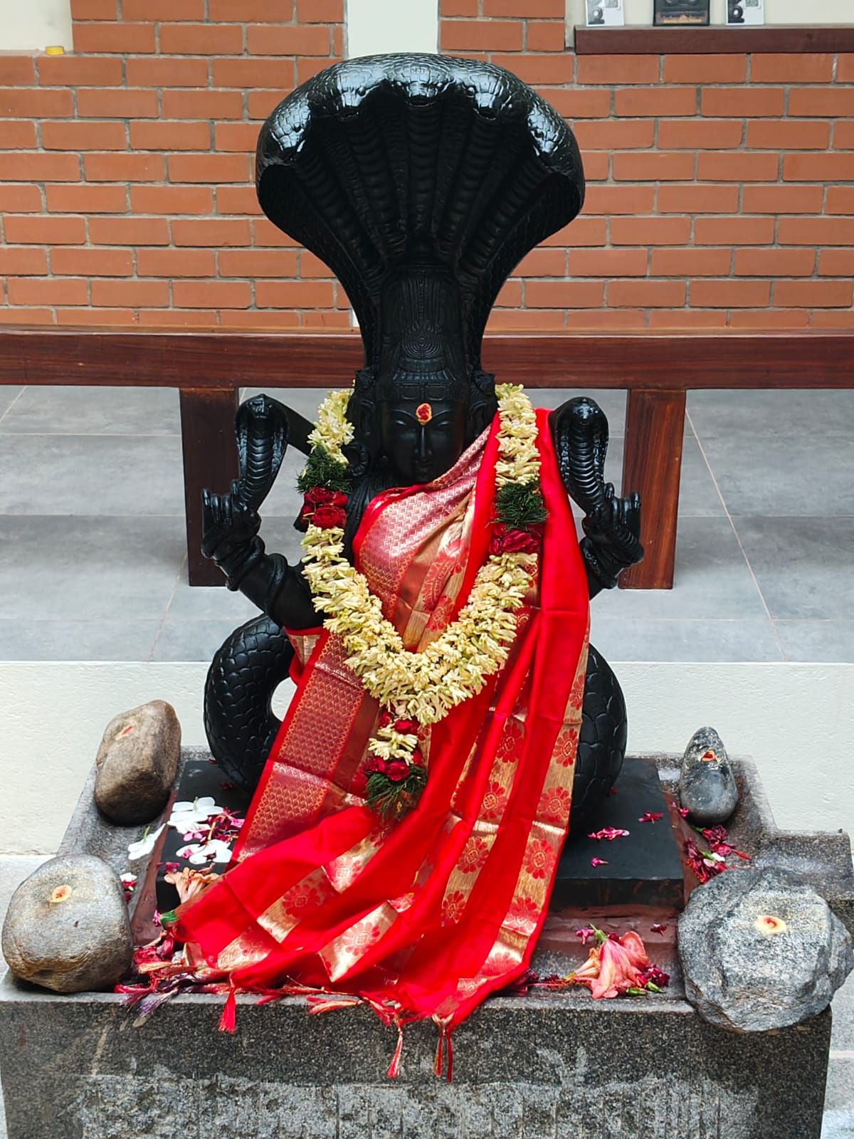 Bala Naga Kanni murti draped in a red silk offering, garlanded with jasmine and roses